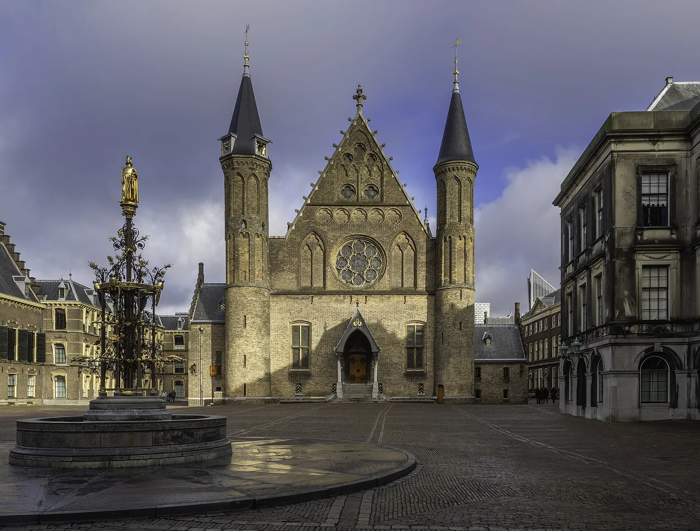 De gotische Ridderzaal met twee torens en een rond glas-in-loodraam, gezien vanaf het plein van het Binnenhof in Den Haag, met een fontein op de voorgrond.