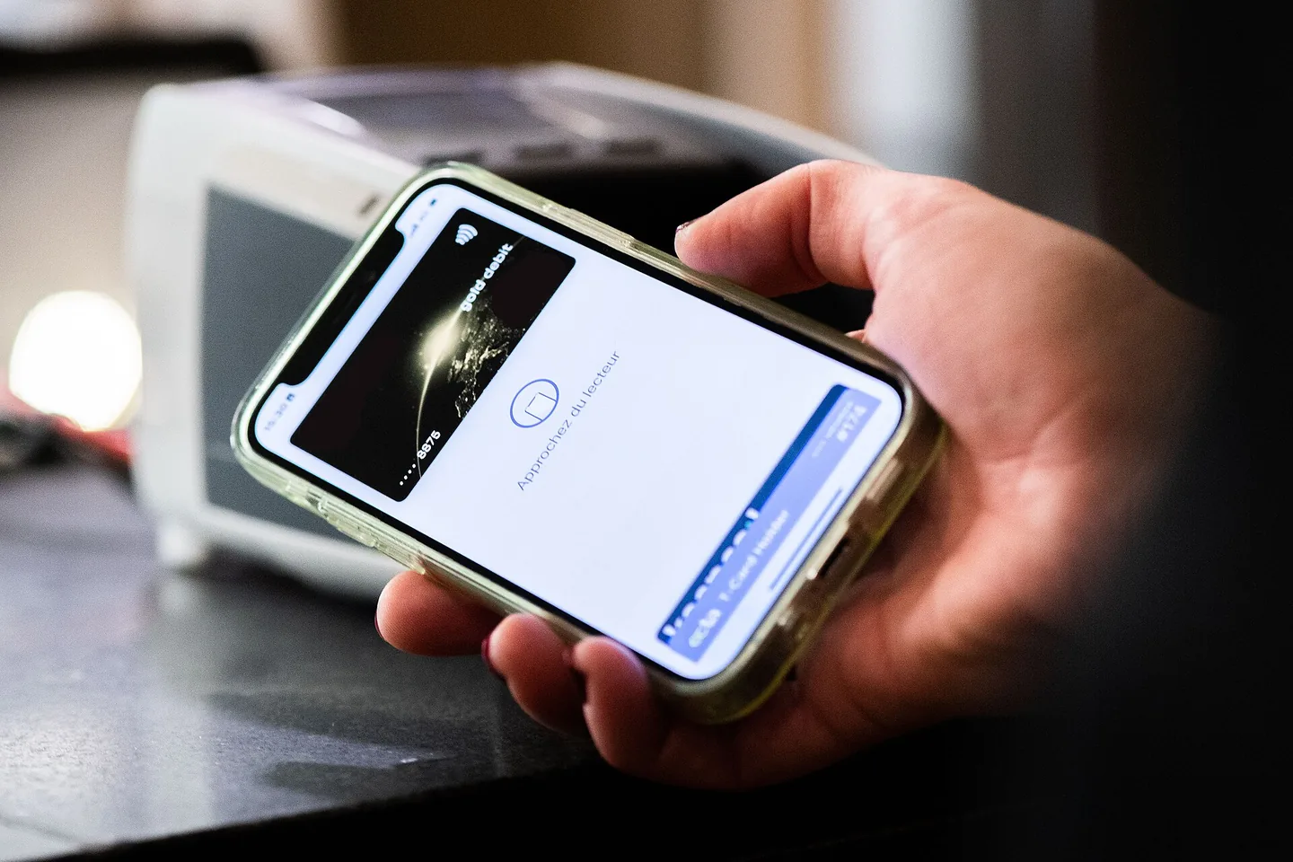 Een hand houdt een smartphone met een digitale betaalkaart op het scherm vlak bij een betaalautomaat.