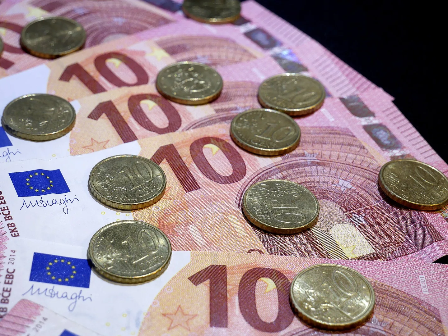Een waaier roze-rode biljetten van 10 euro met de EU-vlag en een handtekening, waarop verspreid goudkleurige munten van 10 cent liggen.