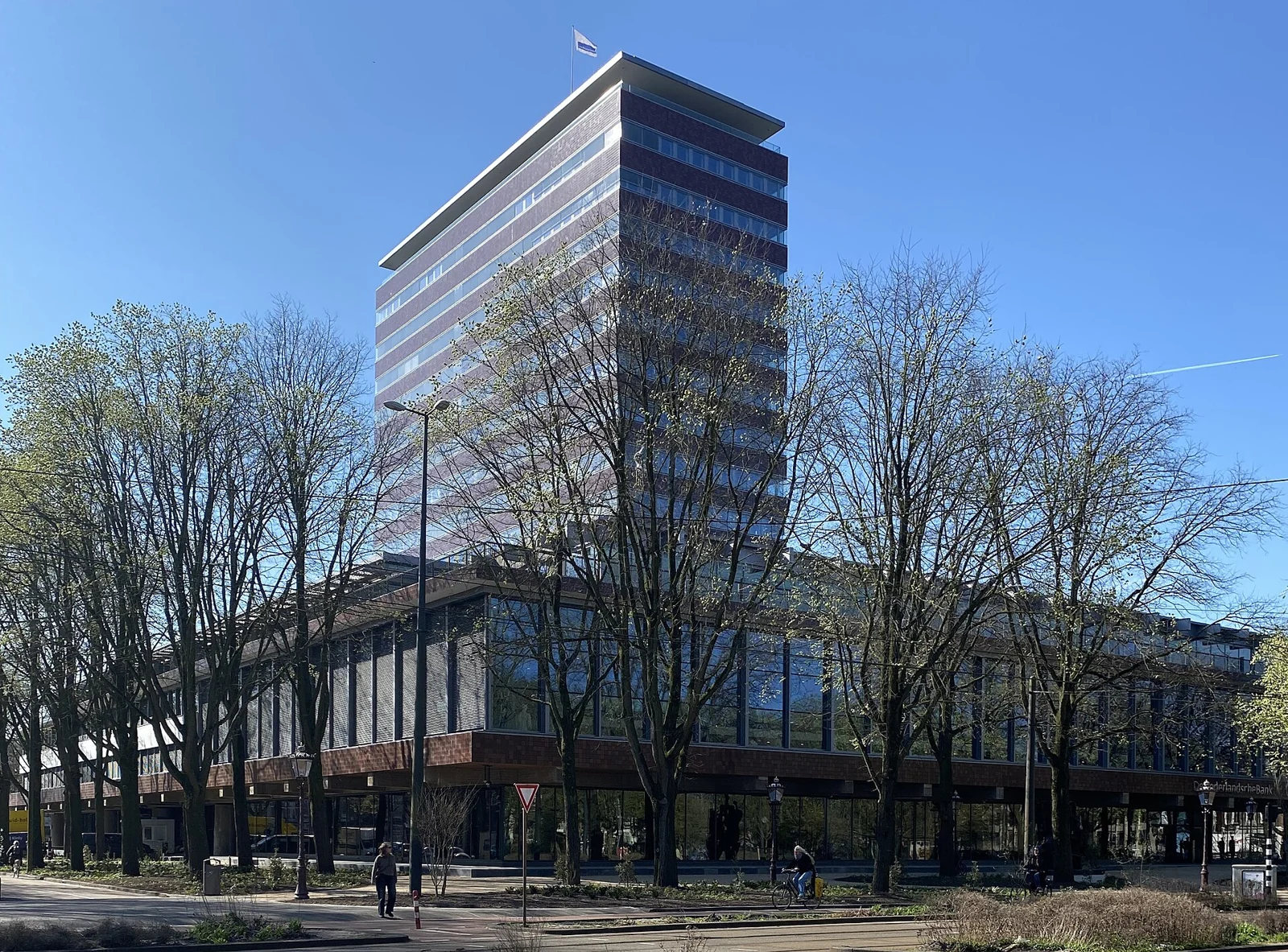 Een hoge glazen toren van De Nederlandsche Bank in Amsterdam, met bomen op de voorgrond.