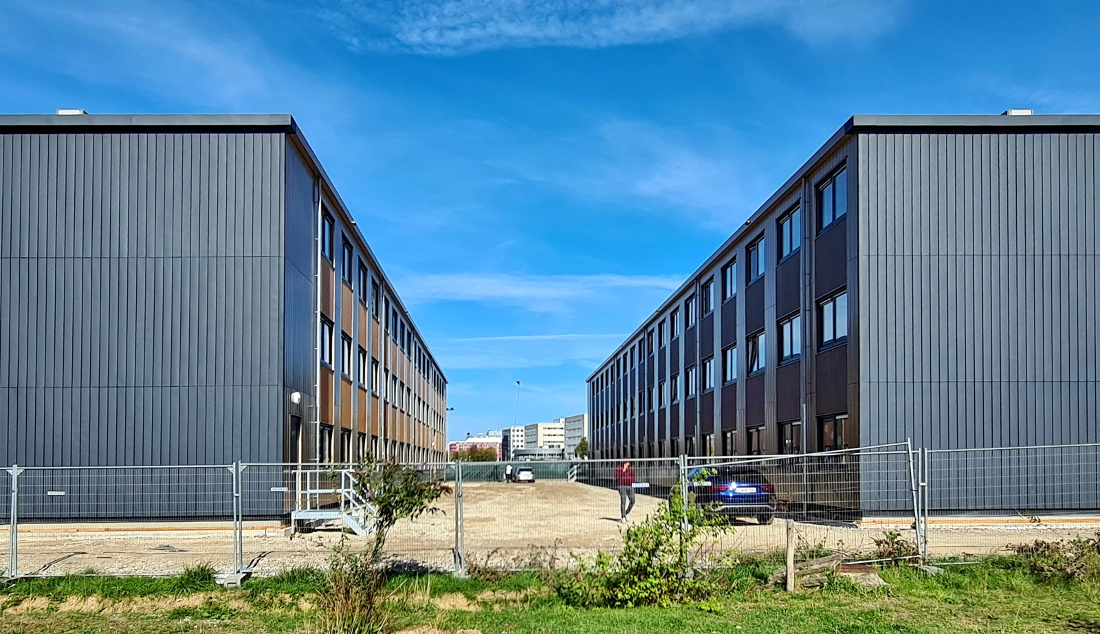 Twee moderne woongebouwen naast elkaar, met een pad en gras op de voorgrond.