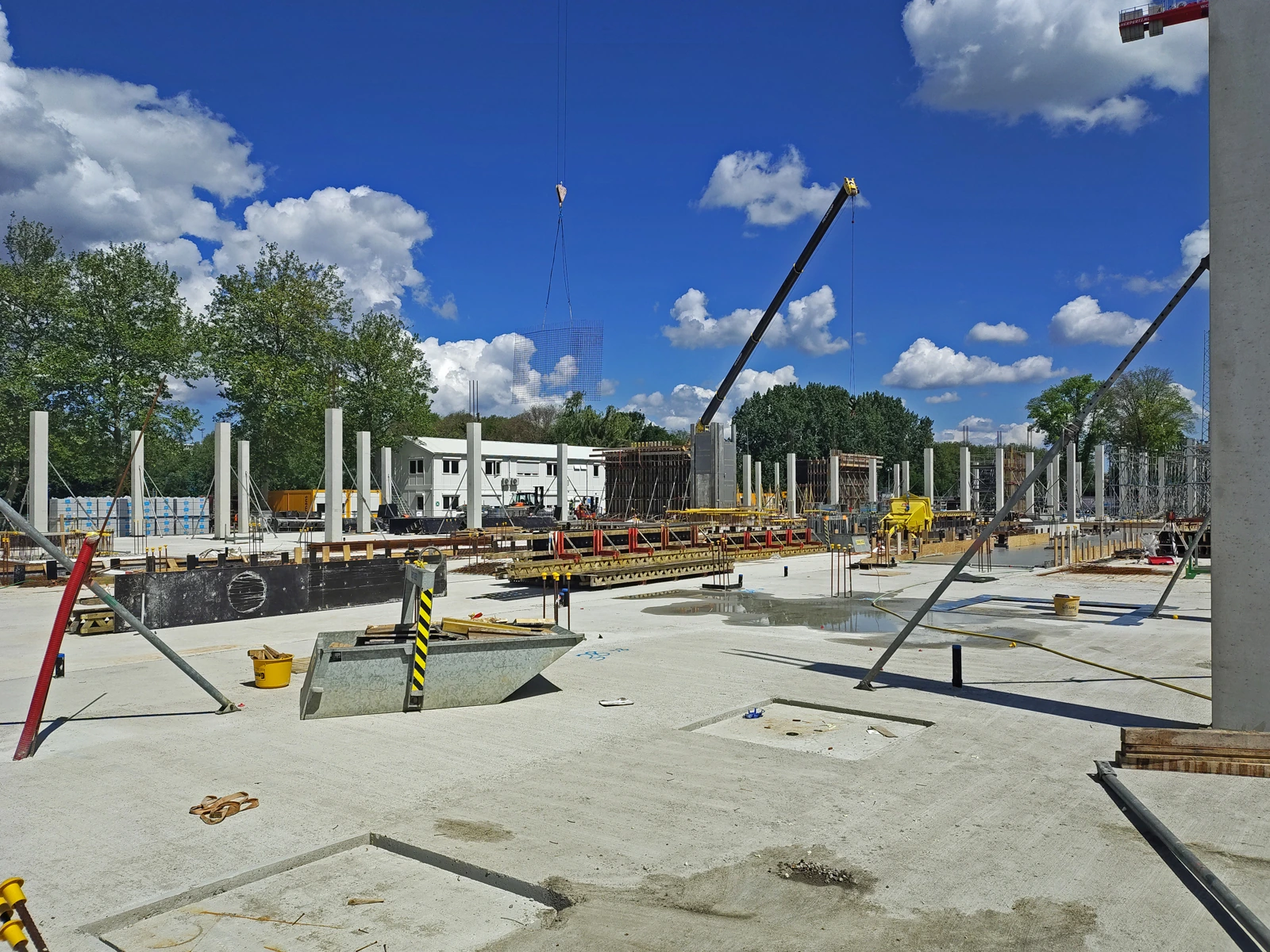 Bouwplaats met betonvloeren, houten bekisting en bouwkranen.