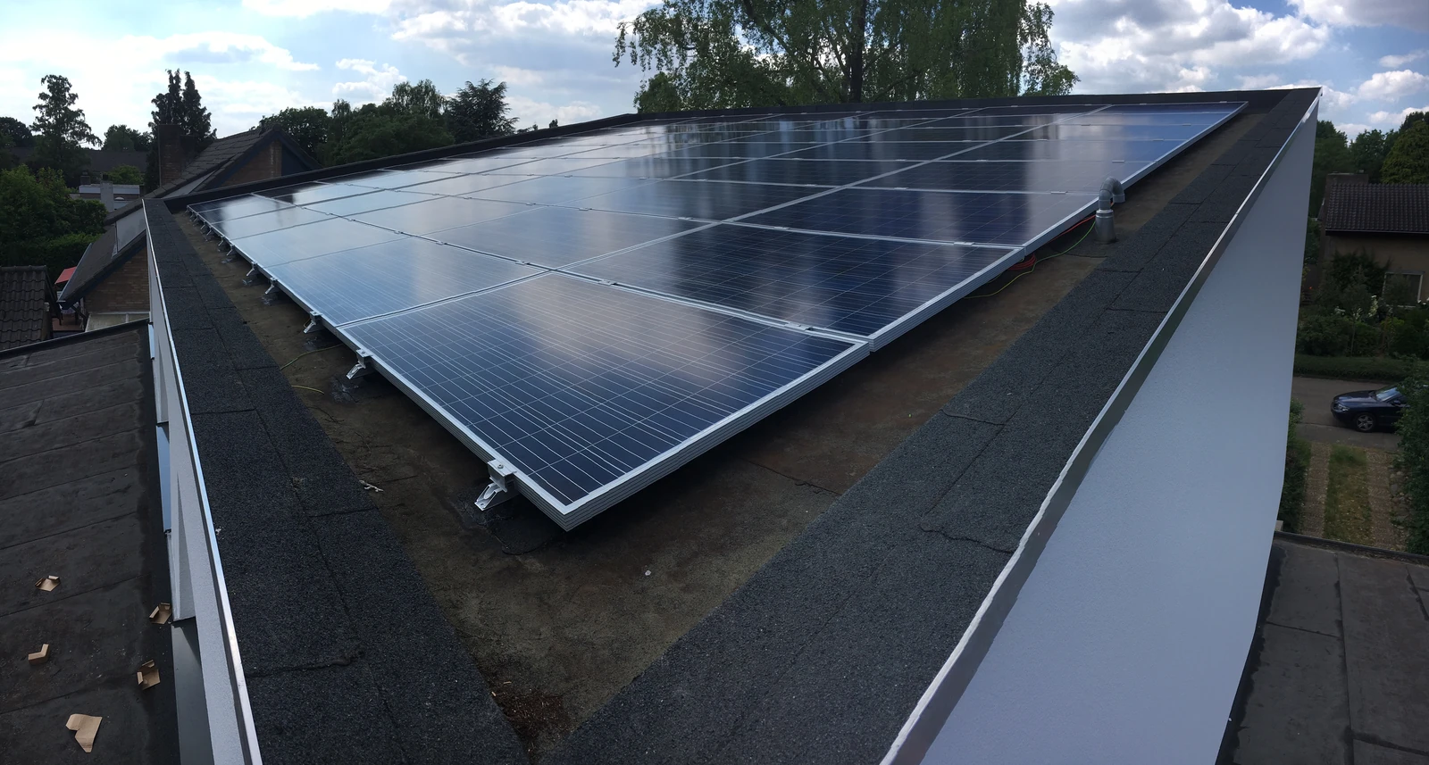 Zonnepanelen op een plat dak, met bomen op de achtergrond.